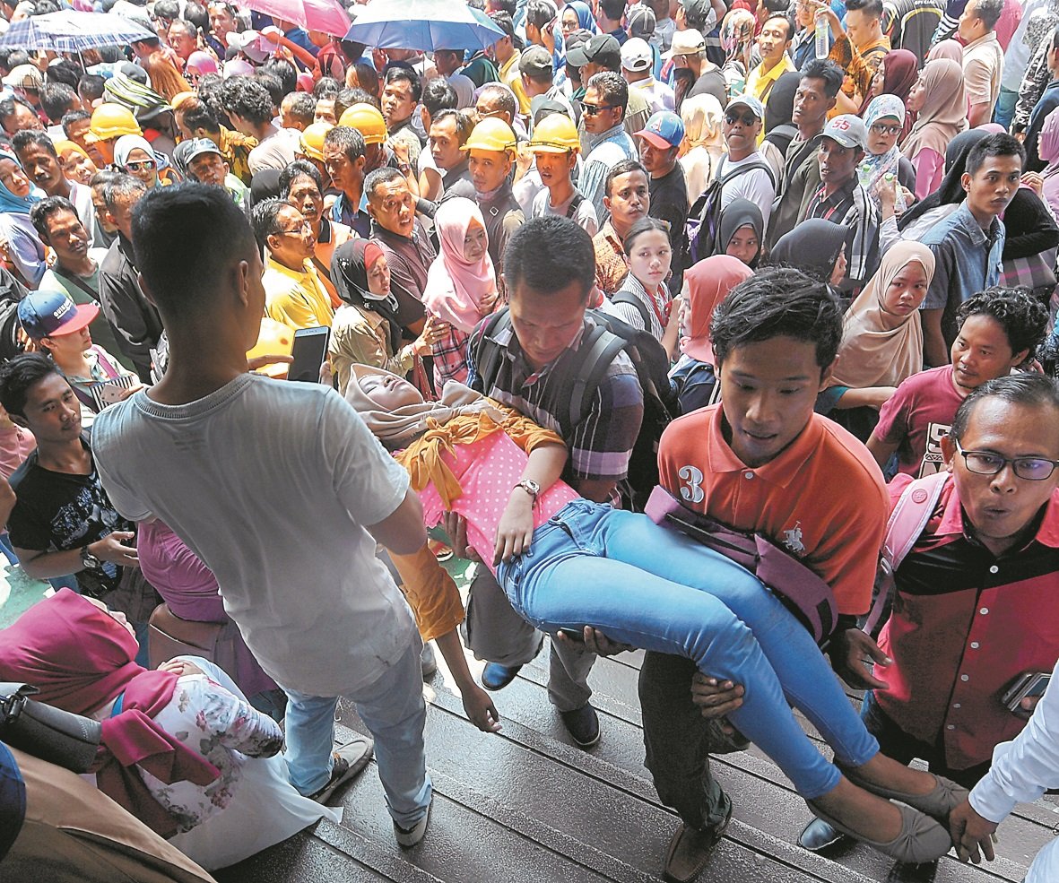 一名印尼女子疑体力不支晕倒，现场热心人士将她抱起，抬 离人群。