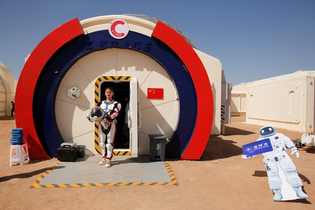 一名工作人员在模拟火星生存基地的范围，身穿模拟太空服、手上拿著头盔，让记者拍照。-路透社-