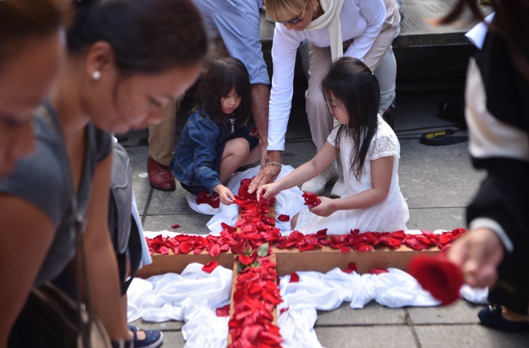 澳洲悉尼的耶稣受难日纪念活动上，女孩们在木质十字架铺上红色的玫瑰花瓣。和全球各地的纪念活动一样，悉尼街头也重演耶稣钉十字架受难的情景。