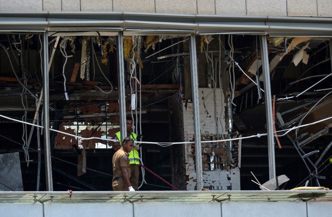 斯里兰卡警察站在科伦坡香格里拉大酒店餐厅区调查，一旁的窗户因遭爆炸波及，只剩下一副残骸。-法新社-