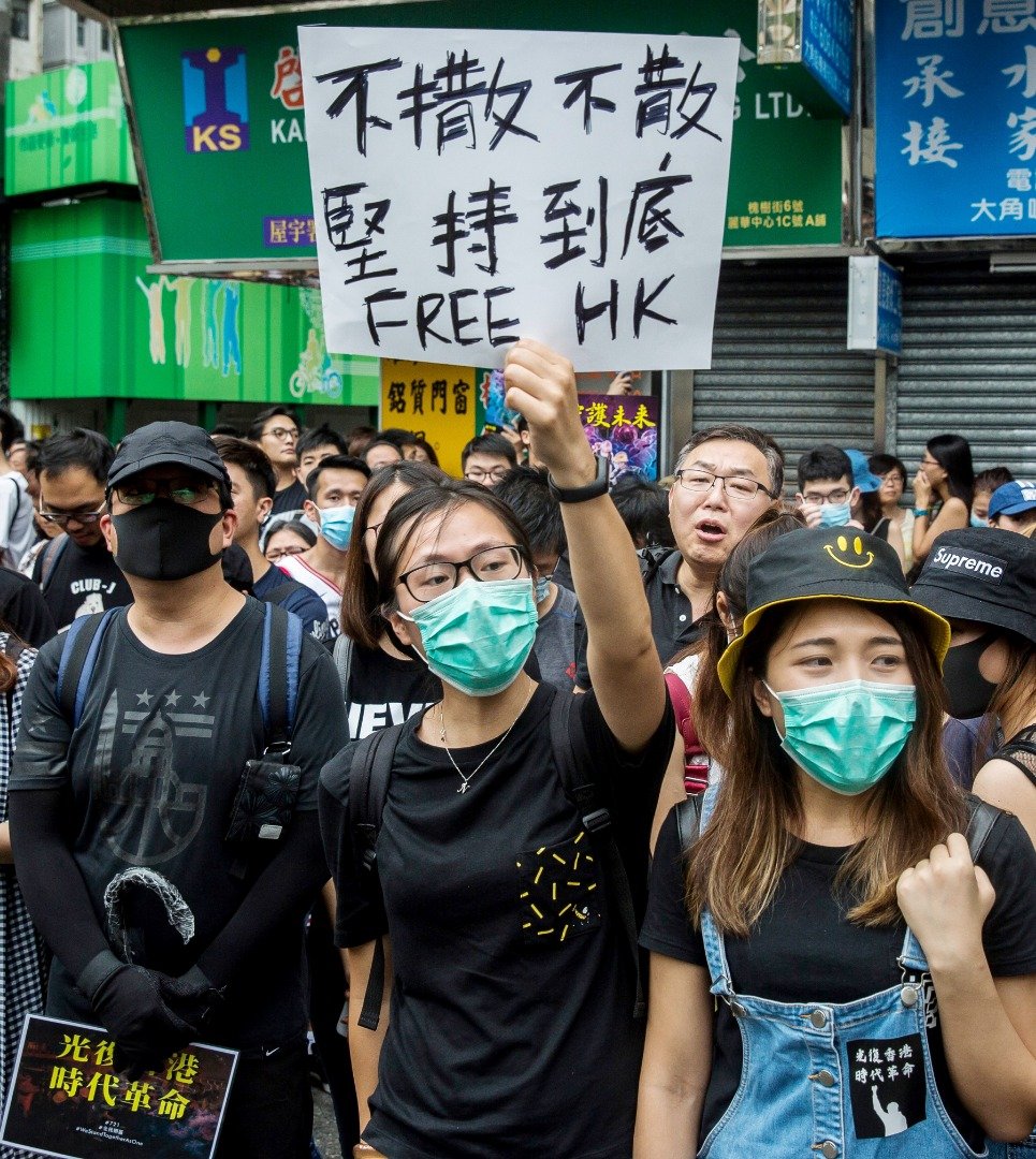 身穿黑衣、戴著口罩的示威者，举著写有“不撤不散、坚持到底”标语的纸板。此次游行的宗旨为，要求香港政府撤回《逃犯条例》修订等5大诉求。