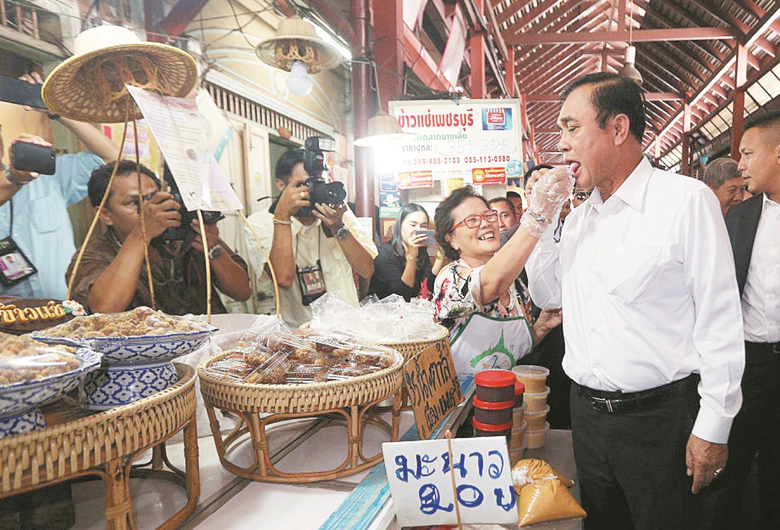 泰国首相巴育（右）周五宣布，接受公民力量党的提名，在来临的大选中竞逐寻求连任。这是巴育周四到访位于曼谷的南龙传统市集，一名小贩热情的给他品尝小吃。