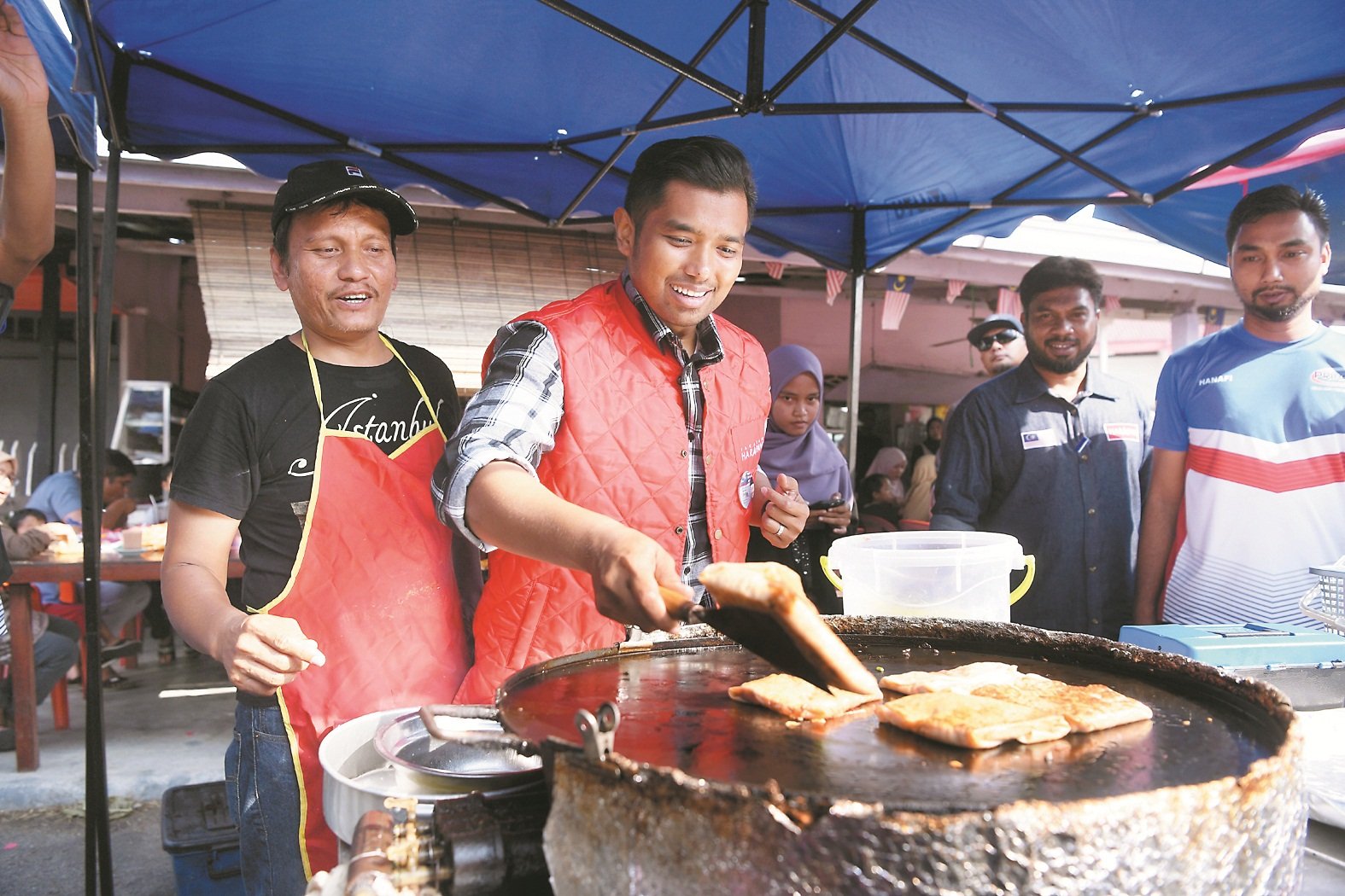 莫哈末艾曼（左2）早上走访峇玲珑早市时，与小贩亲切互动，甚至亲自动手煎饼，令现场充满欢乐。