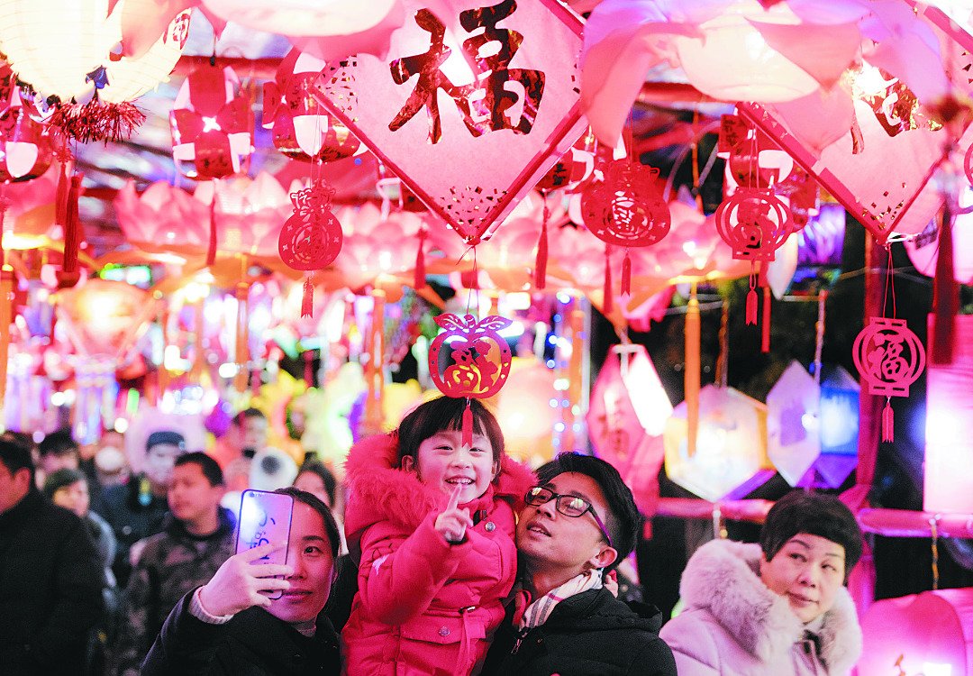 武汉市江岸区百步亭社区第19届元宵灯展周一开幕，超过1万盏自制的主题花灯将社区志愿广场和文化长廊装扮一新。这是家长带著孩子在长廊上观赏花灯，场面温馨。
