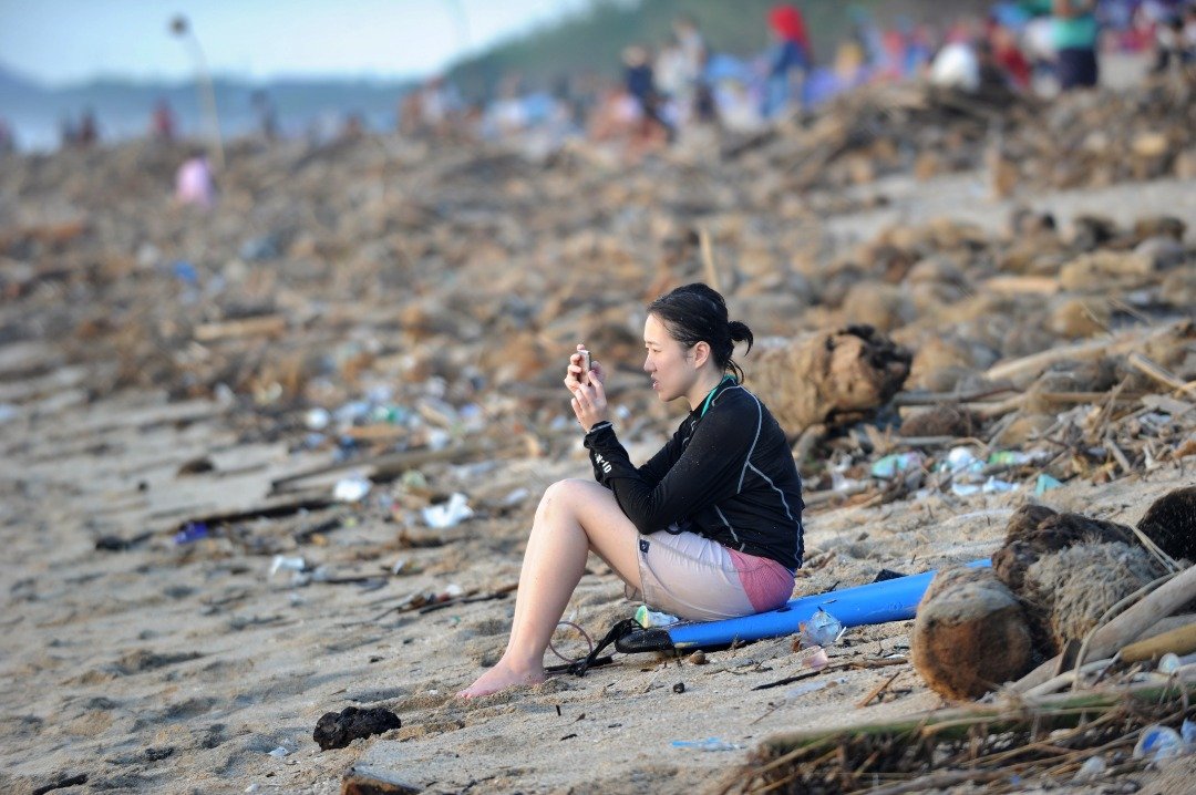 为了解决海洋垃圾问题，印尼政府采取一系列措施，如：建立塑料垃圾循环系统等促进垃圾回收的项目，还要加强公民环保意识。这是一名游客在巴厘岛库塔海滩上使用手机，其身边被冲上岸的垃圾围绕著。