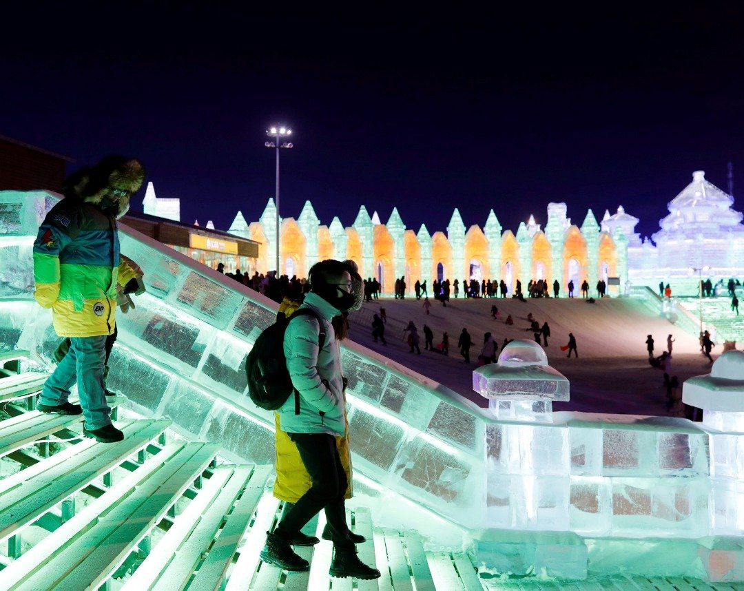 几名游客在彩色灯光照射下的冰雕阶梯上走动，由于气温低，游客们均将自己裹得严实，穿戴著厚重的御寒服装。