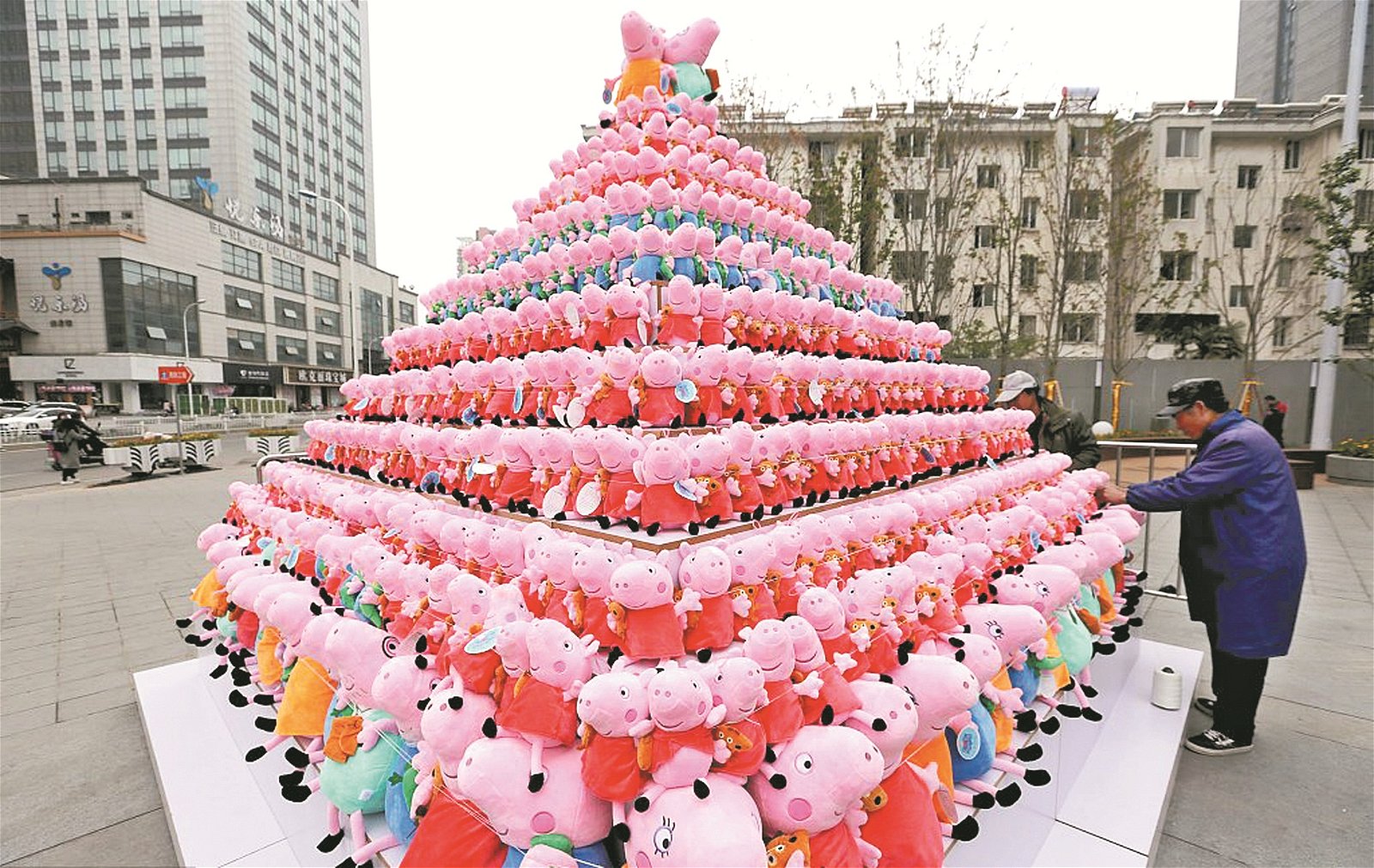 一名位于江苏淮安的商家正进行著促销活动，商家在闹市区中奖数百个“小猪佩奇”的绒毛娃娃叠放成金字塔的形状，十分引人注目，夺人眼球。