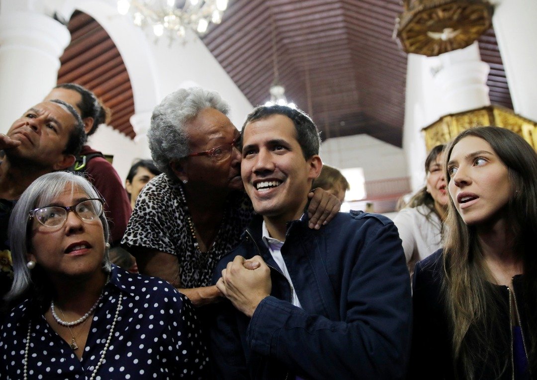 日前自立为临时总统的瓜伊多（中）周日与妻子罗萨莱斯（右），和母亲马克斯（左）周日抵达加拉加斯一所教堂，出席弥撒及悼念逾20名在反政府示威中身亡的人士时，受到一名热情的支持者亲吻。