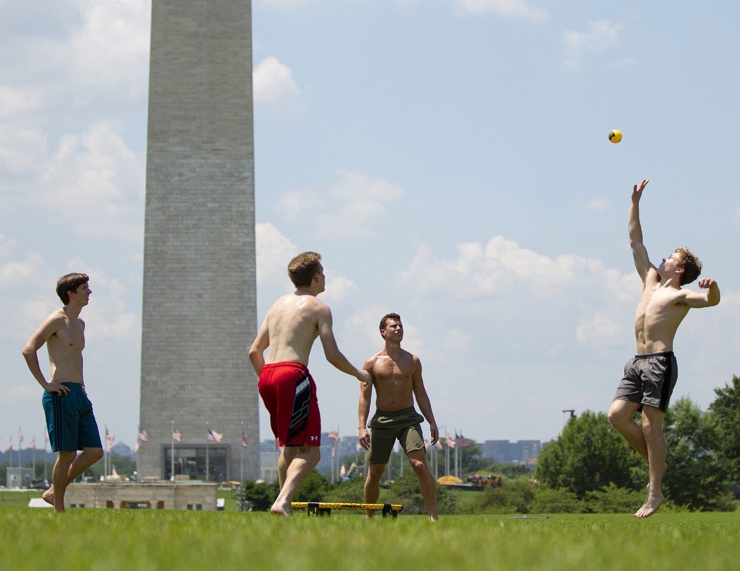 几名青少年在烈日照耀的天候下，脱去上衣在华盛顿国家广场前的草地上玩圆网球。已办了19年的纽约铁人三项比赛，今年因碰上热浪来袭首次取消。
