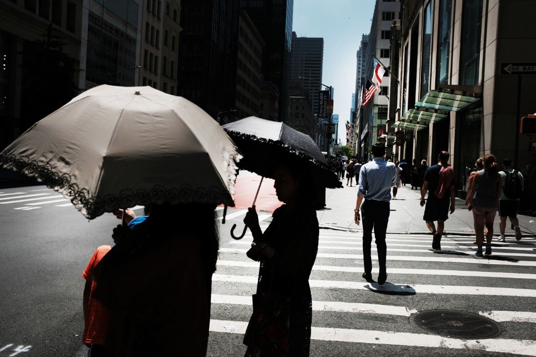 纽约市街头的女士撑开伞，遮挡炙热的阳光。热浪笼罩美国多个地区，超过100个地区周末预计将迎来破纪录的高温。
