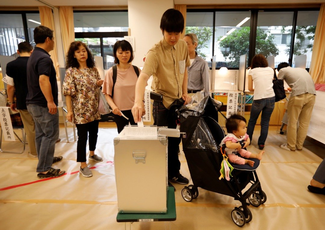 东京一名年轻选民推著还在襁褓中的婴儿，在票站内投票。选前民调显示，日本这次参院改选投票率将明显低于50%。