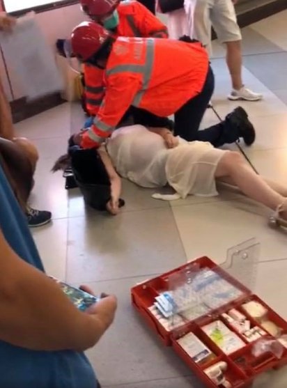 孕妇表情痛苦地躺在地上，一旁的救护人员正在为她包扎，孕妇还不断啜泣。