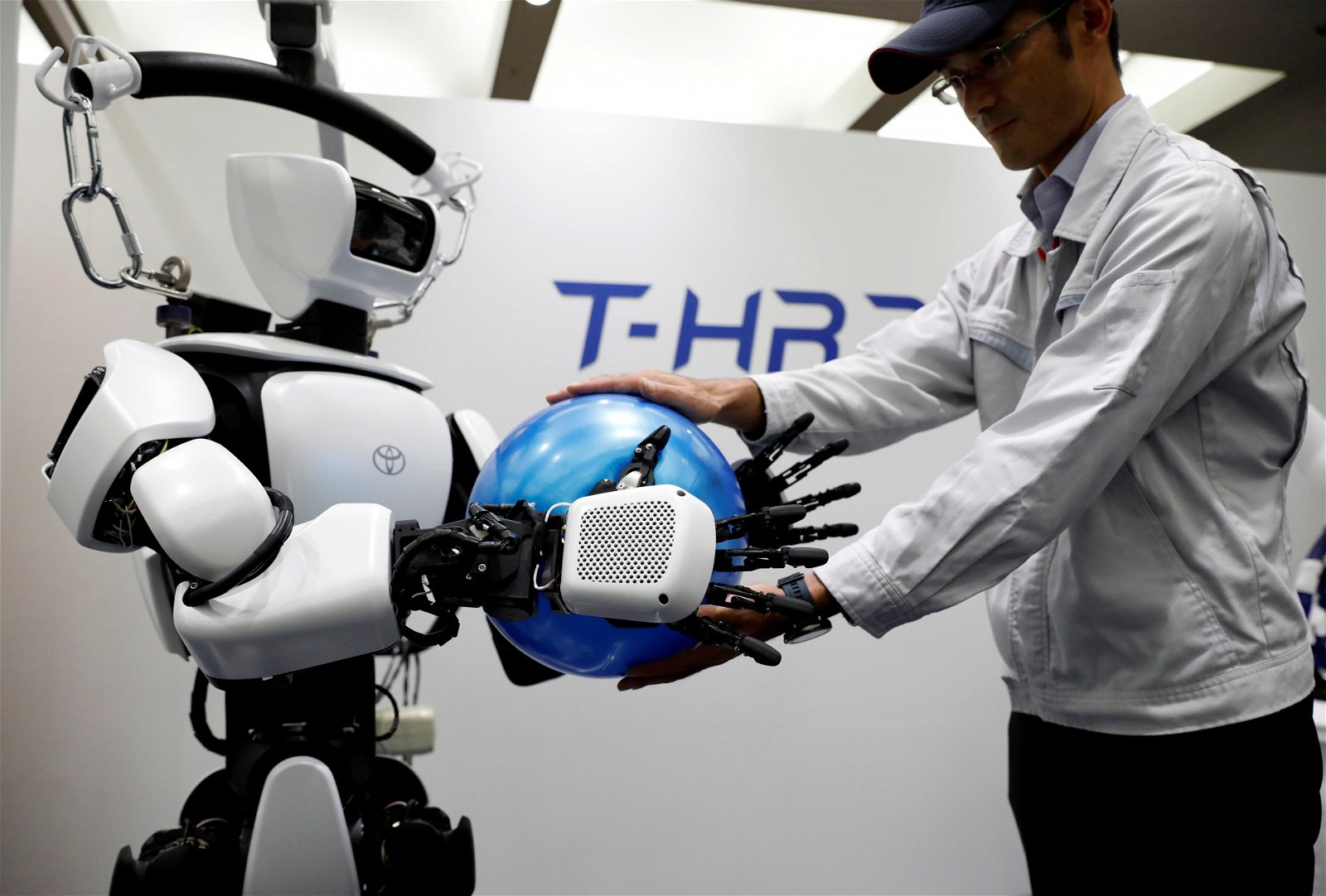 丰田汽车公司旗下的“T-HR3”仿人机器人正示范将手中的球，交给丰田汽车工作人员。