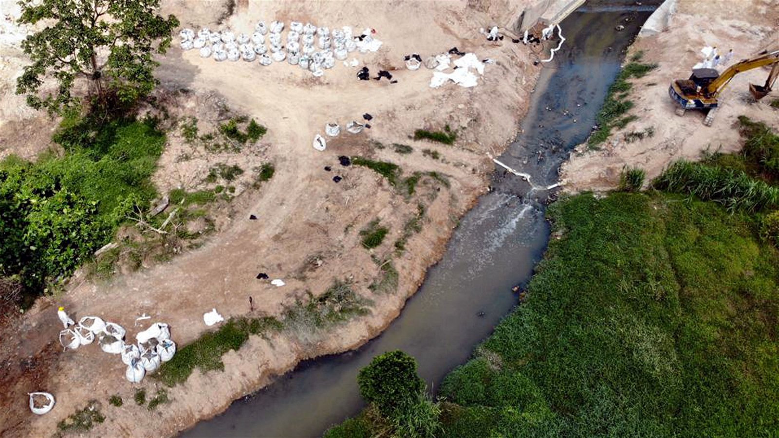 今年3月份，巴西古当因金金河污染事件一夜之间成为全国人民关注的焦点，金金河也在短时间内获政府投入大笔资金和人力，已求在最短时间内有效清理河流内化学废料。图中河流是化学污染事件爆发时的情况，从高空俯视，可见河面变黑。河岸边的白色袋子内所装置的则是工作人员从河内打捞出来的化学废料。