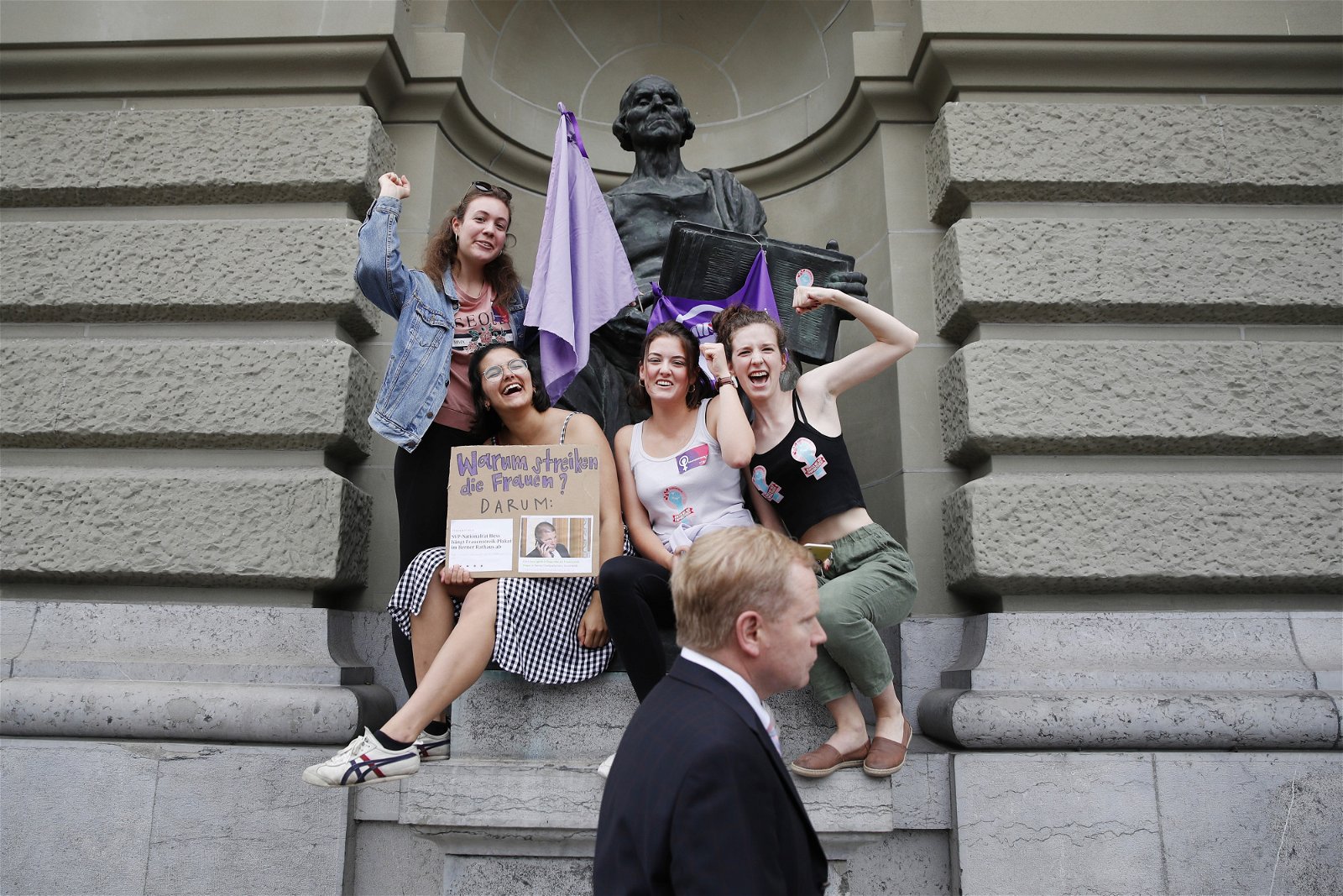 参与示威的女性，在联邦议会前的雕像挂起紫色旗帜，举起拳头展现女性的力量，要求男女平权。