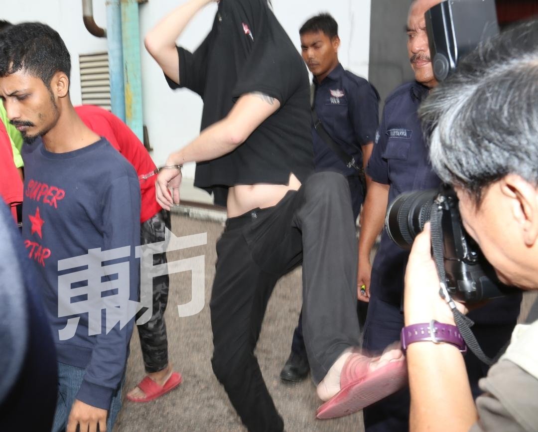 黑衣嫌犯被带离推事庭时，企图用脚攻击媒体，所幸被警方阻止。（摄影：刘维杰）
