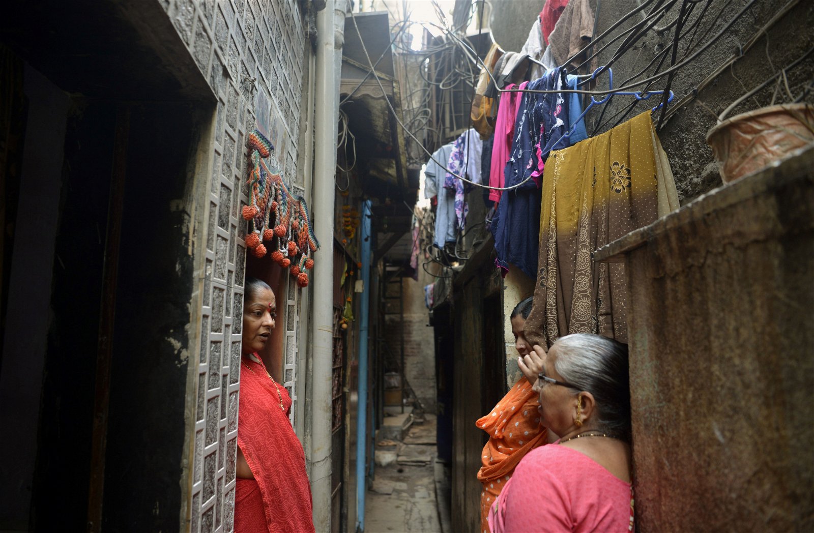 生活在达拉维平民窟的妇女，在房屋之间的狭窄小巷中闲话家常。印度政府打算将该平民窟打造成新加坡式的飞地经济。有支持者认为，该计划将有助提升人民生活水平。