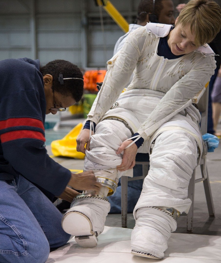 麦克莱恩在地面训练时，在工作人员的协助下穿上太空服。太空服实际上由几部分组件组装而成，方便适应各太空人的身形，而且还需考量微重力环境可能会使身材产生变化，因此一套完全合身的太空服至关重要。