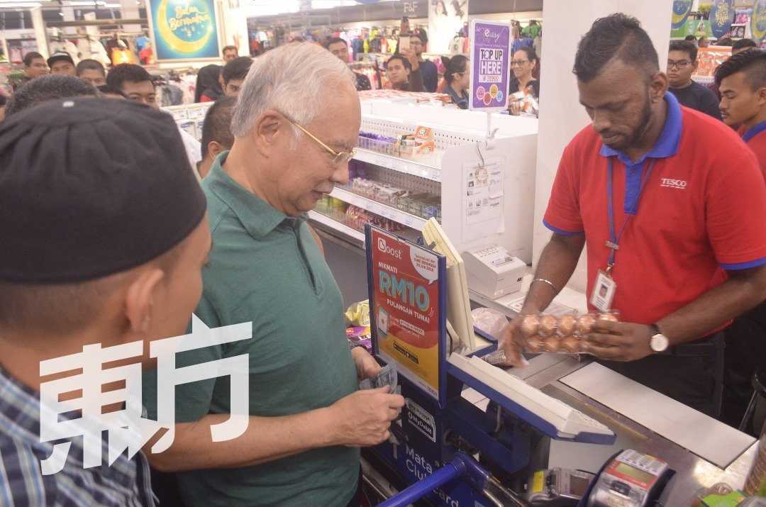 纳吉（左2）在结算柜台，以100令吉现金支付所购买的用品费用。