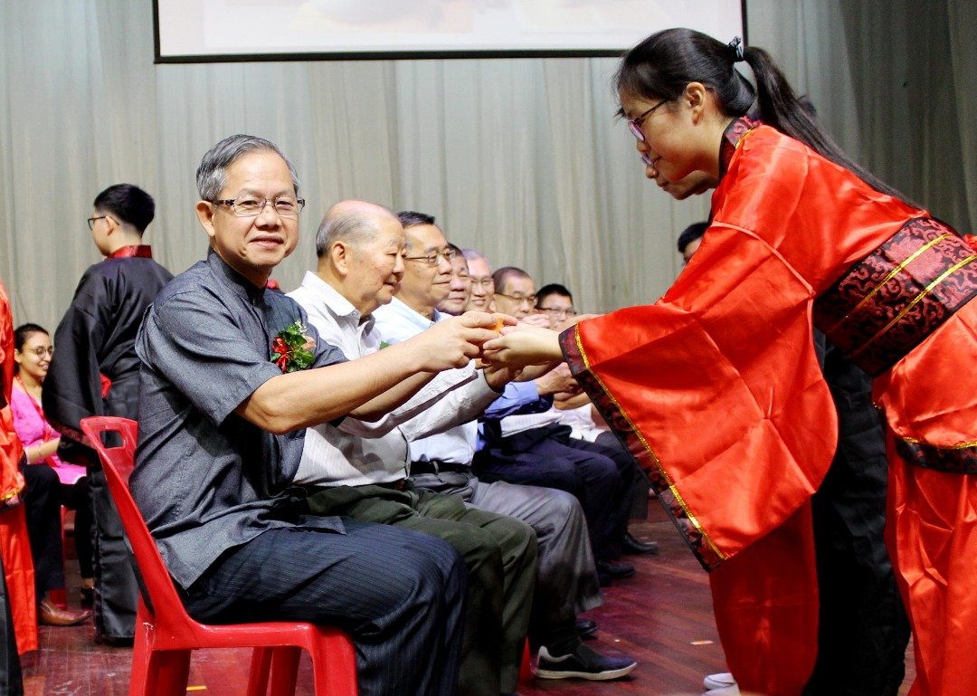 李文材（左）在弟子规活动的敬茶仪式上，双手接过学生敬上的一杯茶。