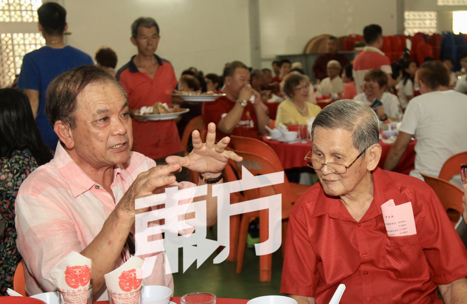 邱财加（左）在午宴席上与陈兴交流，了解希望之谷福建同乡会面临许多会员年迈，而会所久未翻新的处境。（摄影：甘月仙）