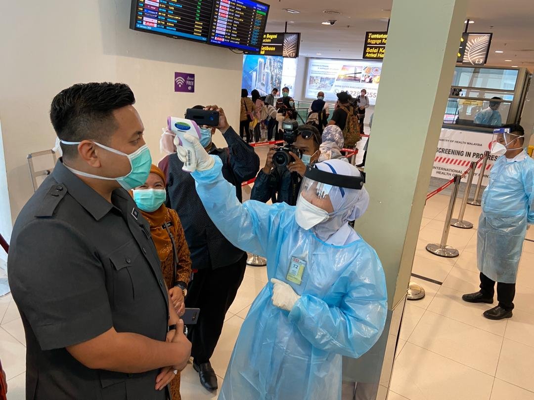 阿菲夫（左）在槟城国际机场亲身示范，接受医护人员的体温检测。