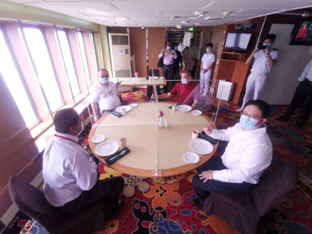 陈德钦（左3）示范在邮轮上用餐，与同桌者隔著透明塑料板。