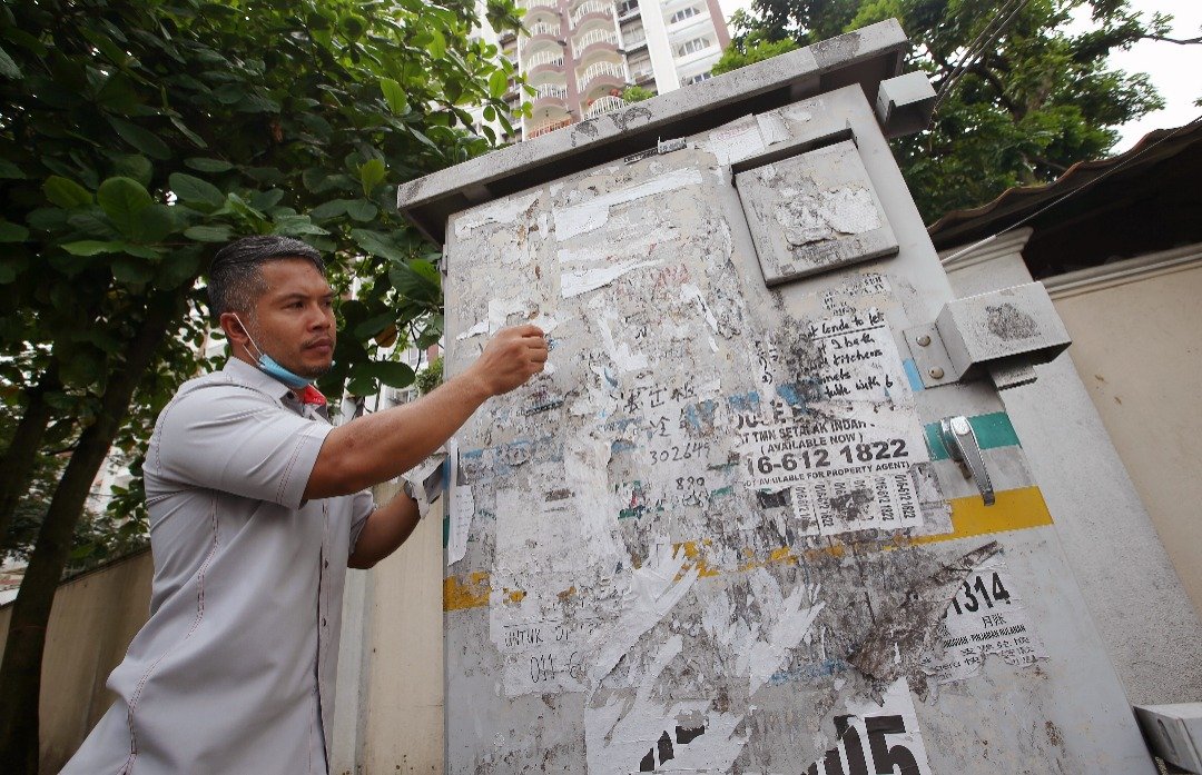 非法街招不仅破坏公物也妨碍市容，图为阿末依努正移除电箱上的非法广告招贴。摄影：骆曼