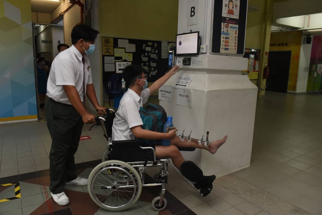 负伤学生坐在轮椅上伸手扫描其学生证，打卡报到。
