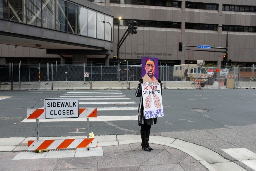 示威者拿弗洛伊德的画像和口号，在明尼苏达州明尼阿波利斯市亨内平县已被封锁的政府大楼外抗议。（图取自路透社）