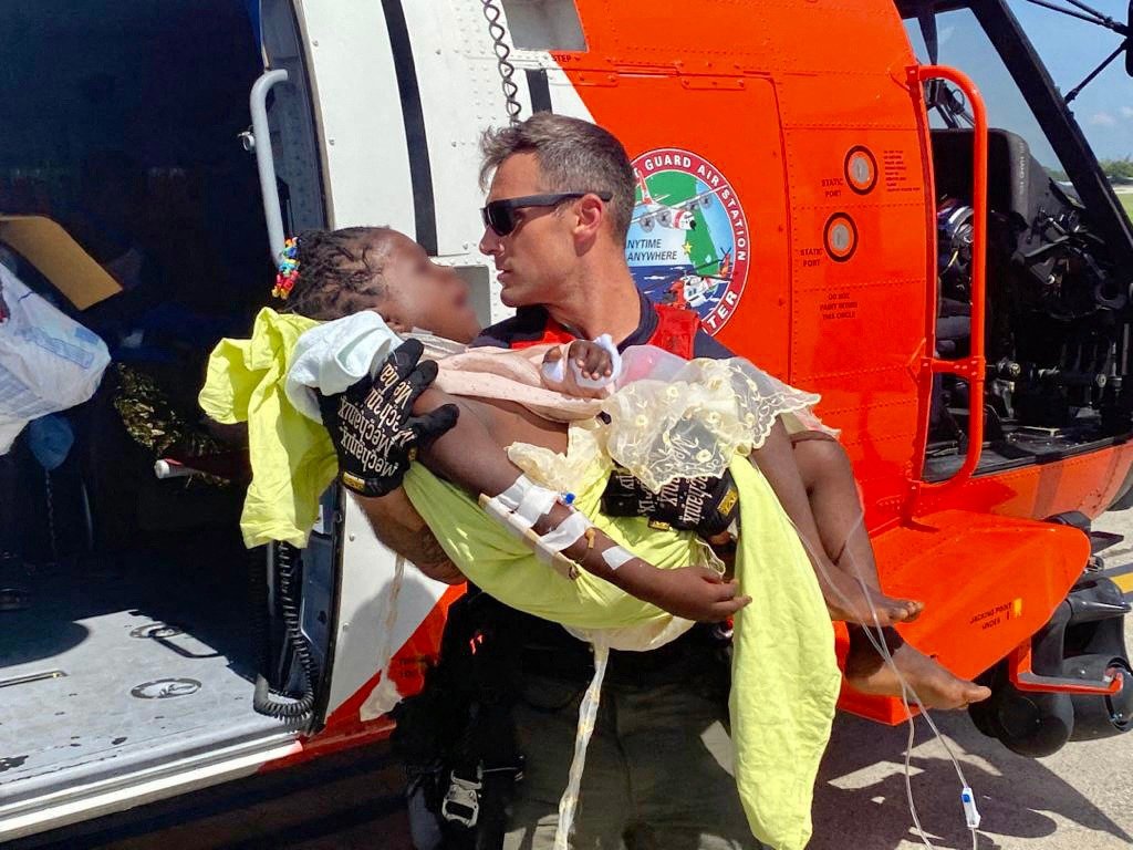 一名美国海岸防卫队机组人员，将一名受重伤的儿童抱下直升机，送往太子港当地紧急医疗服务机构。（图取自美国海岸防卫队 / 法新社）