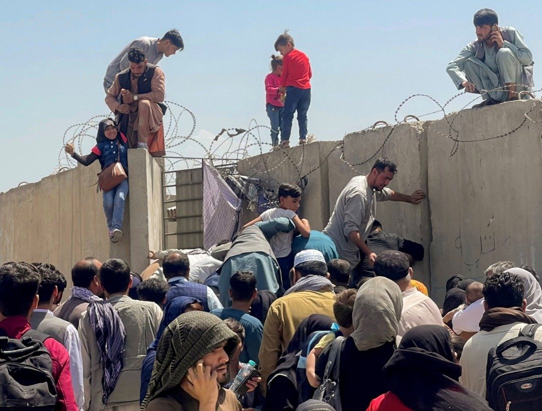 阿富汗政府周日垮台，周一仍有群众尝试进入喀布尔国际机场，而一名男子拉著一名女孩的手，希望能到机场内。（图取自路透社）