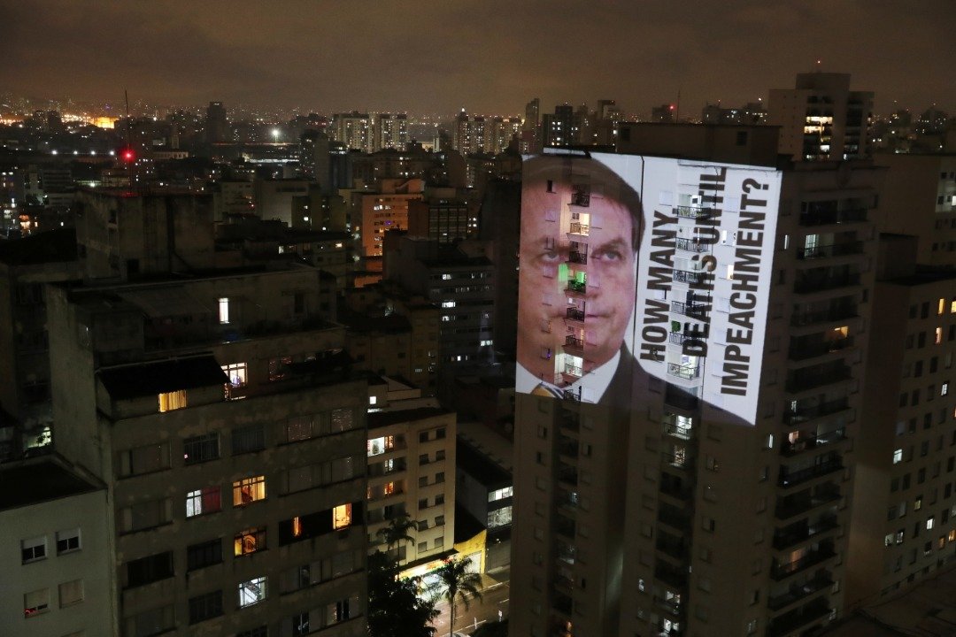 在圣保罗市圣西西利亚区，当地时间周五，有人抗议巴西总统博索纳罗抗疫政策和处理玛瑙斯疫情危机的态度，把其肖像投射在公寓上，写上“弹劾之前还有多少人死”标语。（路透社）