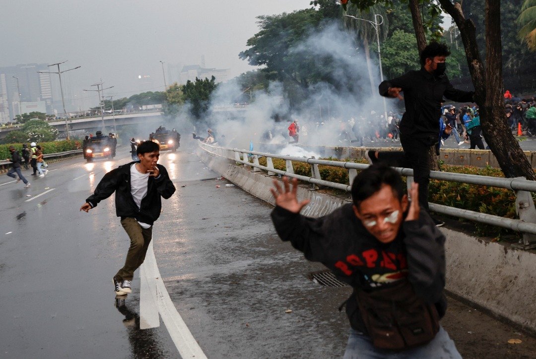 印尼首都雅加达周一迎来一场示威活动，示威者因不满有部长表示延长现任总统任期的想法而上街游行，遭警方使用催泪弹驱赶，为躲避烟雾四散开来。（图取自路透社）