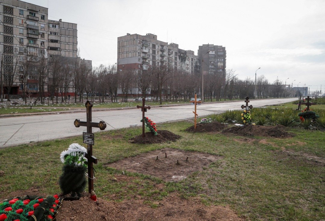 在乌克兰南部港口城市马里乌波尔的公寓旁，可以看到在乌俄冲突中丧生的平民坟墓。（图取自路透社）
