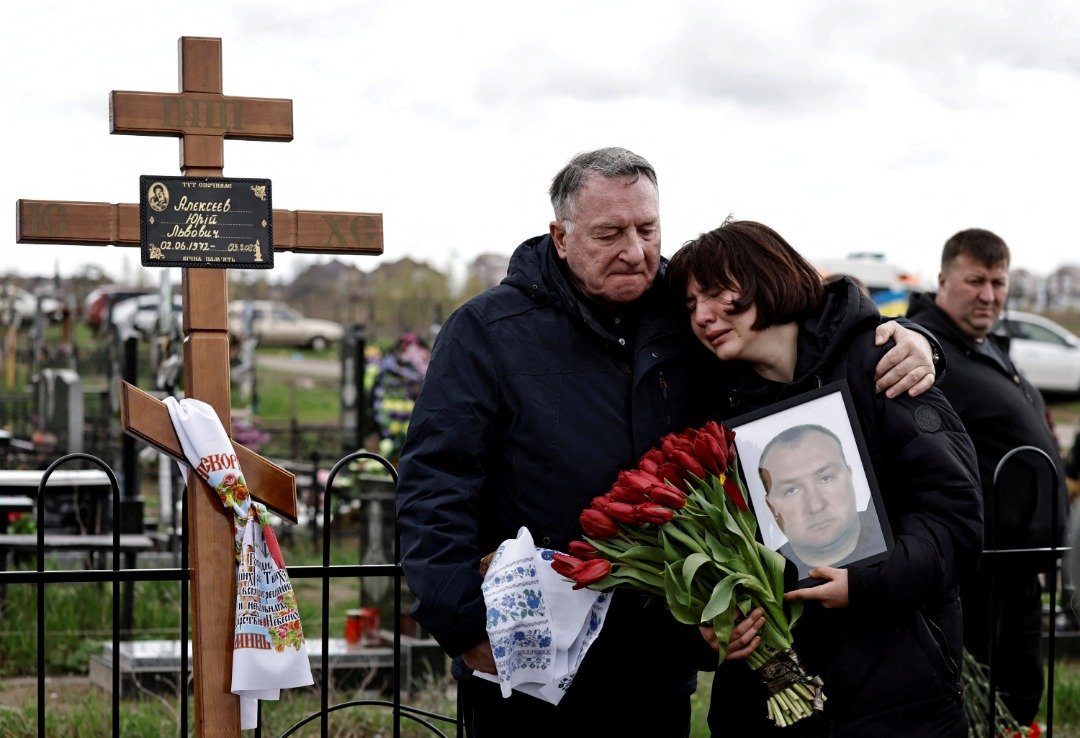 在乌克兰布查镇的一处墓地，13岁的玛丽亚周二拿著她父亲阿列克谢夫的遗照。据阿列克谢夫的家人表示，他是一名领土防卫成员，在俄罗斯入侵期间遭俄军杀害。（图取自路透社）