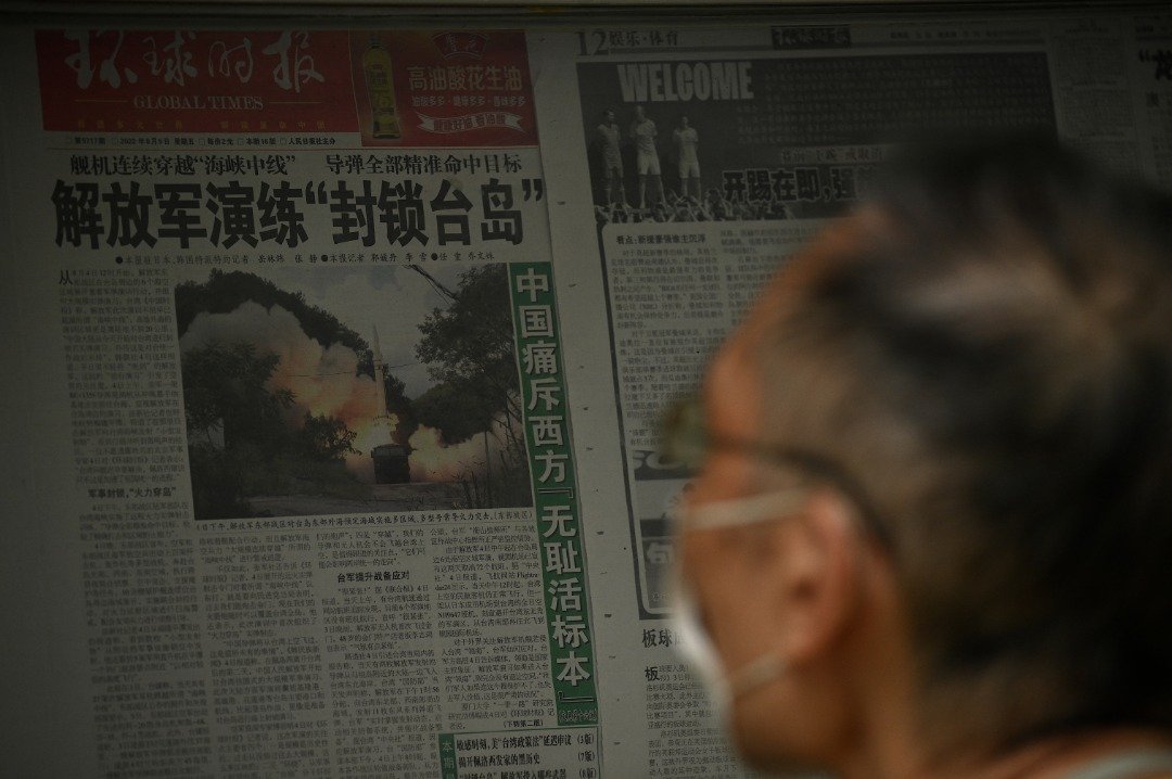 有北京民众周一在一条街道上，阅读有关中国包围台湾军事演习的新闻报导。（图取自法新社）