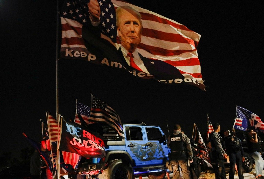 在FBI探员8日晚间搜查特朗普位于佛州的庄园时，特朗普支持者在外举著旗帜，声援特朗普。（图取自路透社）