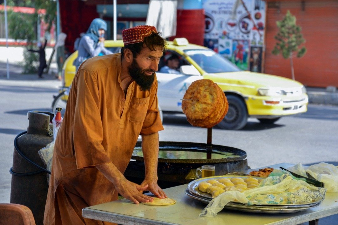 这张拍摄于2022年7月18日的照片，显示坎大哈一名男子在一个摊位上准备早餐。（图取自法新社）