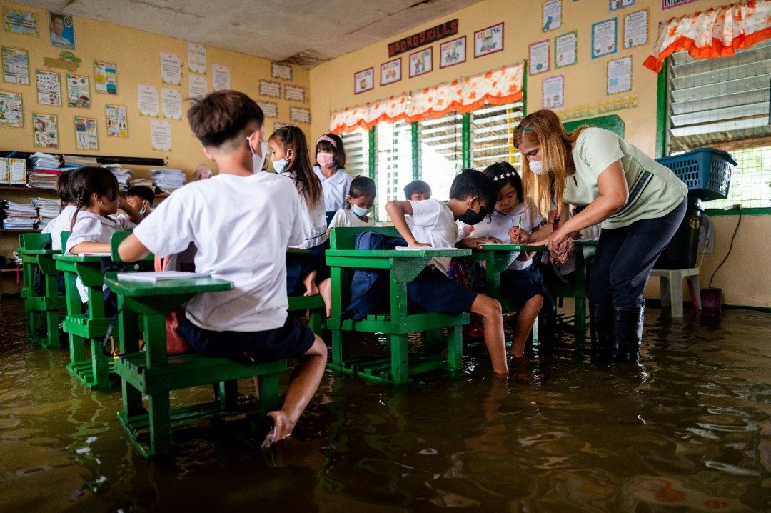 在菲律宾邦板牙省马卡贝贝，一所学校周一在被泛滥河水淹没下开课，教师穿著长筒靴，学生们则赤脚上课。（图取自路透社）