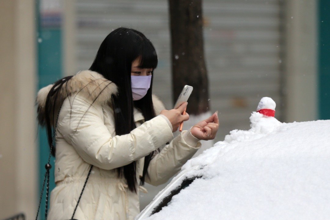周日，西安迎降雪天气，一名年轻女子拍摄车顶的雪人。（图取自中新社）