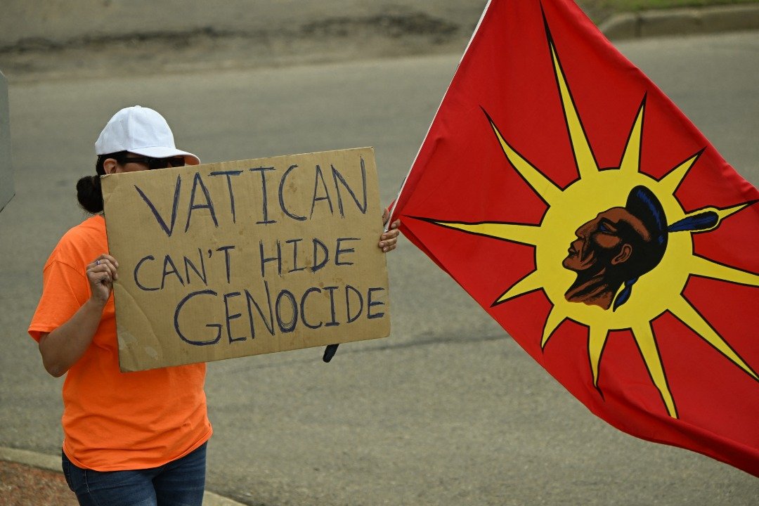 当罗马天主教教宗方济各抵达加拿大埃德蒙顿访问时，一名抗议者举著标语。（图取自法新社）