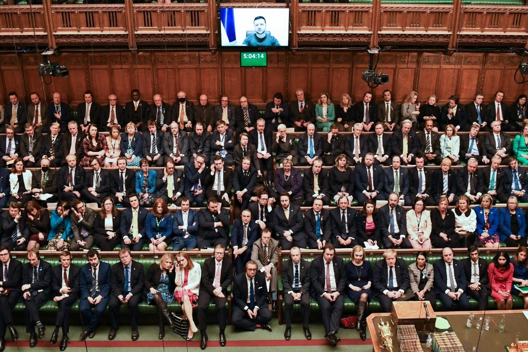 英国国会议员通过实时视频链接，当地时间周二在伦敦下议院聆听乌克兰总统 泽连斯基讲话。英国下议院座无虚席，议员们全神贯注，最后全场起立，报以热烈掌声。（图取自英国国会/法新社）