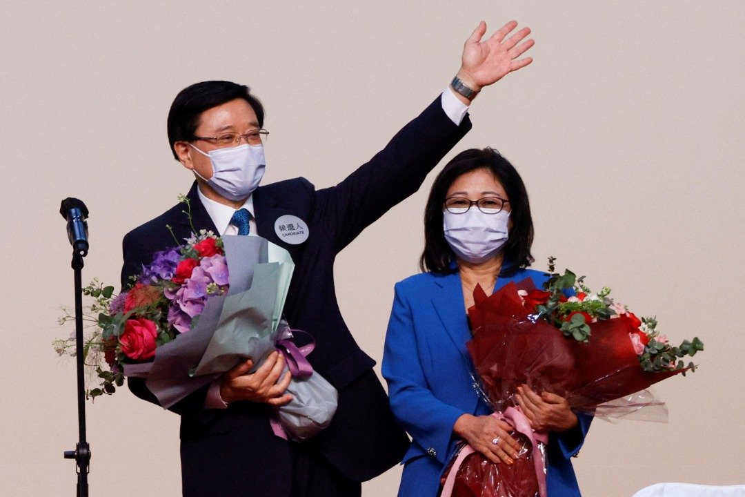 在周日当选香港新一任特首的李家超，与太太林丽婵在台上接受祝贺。（图取自路透社）