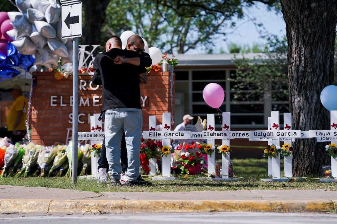 发生枪击案的罗布小学外摆满鲜花和写上遇难者名字的十字架，有民众拥抱一起安慰彼此。 （图取自路透社）