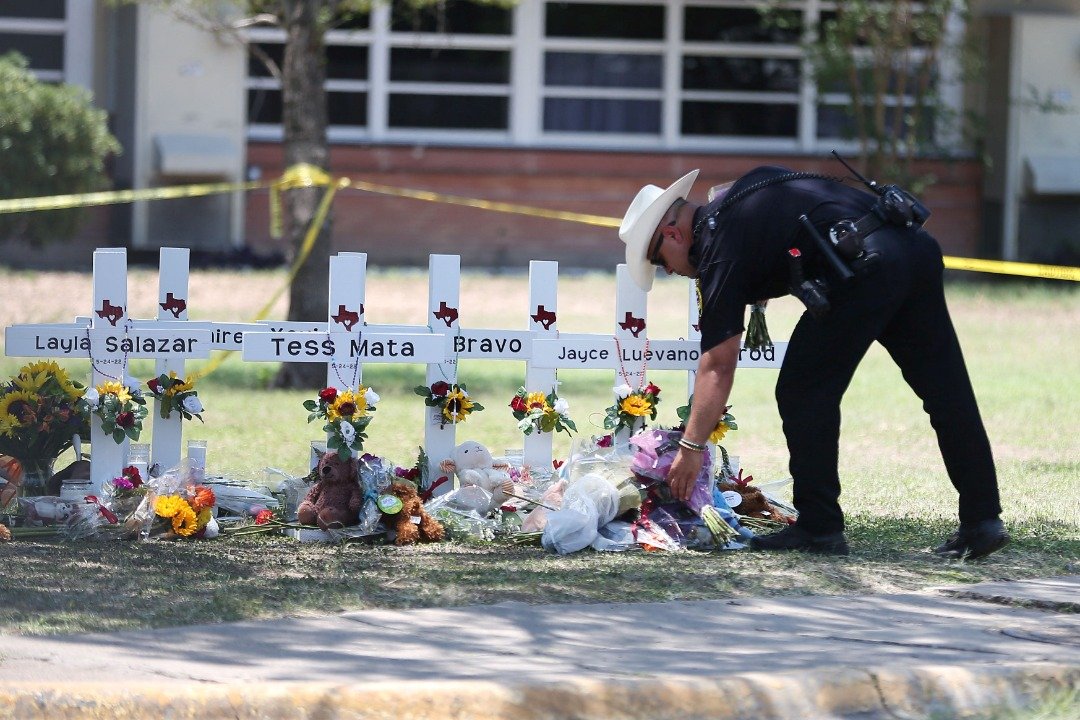 一名警官周四在发生枪击案的罗布小学临时纪念处，向遇难者献上鲜花致意。 （图取自路透社）