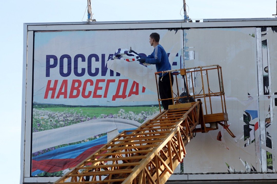 在乌军最近收复的赫尔松市，一名工人当地时间周一撕掉了写著“俄罗斯永远在这里”的广告牌。（图取自法新社）