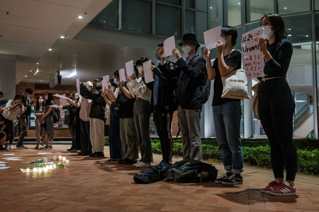 在香港大学的校园内，一群学生周二举著标语和白纸，声援中国反对严格防疫限制和要求更大的自由。（图取自法新社）