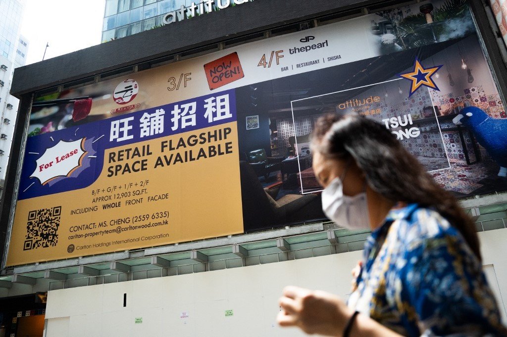 一名妇女上周六走过香港九龙区一家空置的商店，上面挂著出租广告牌。（图取自法新社）