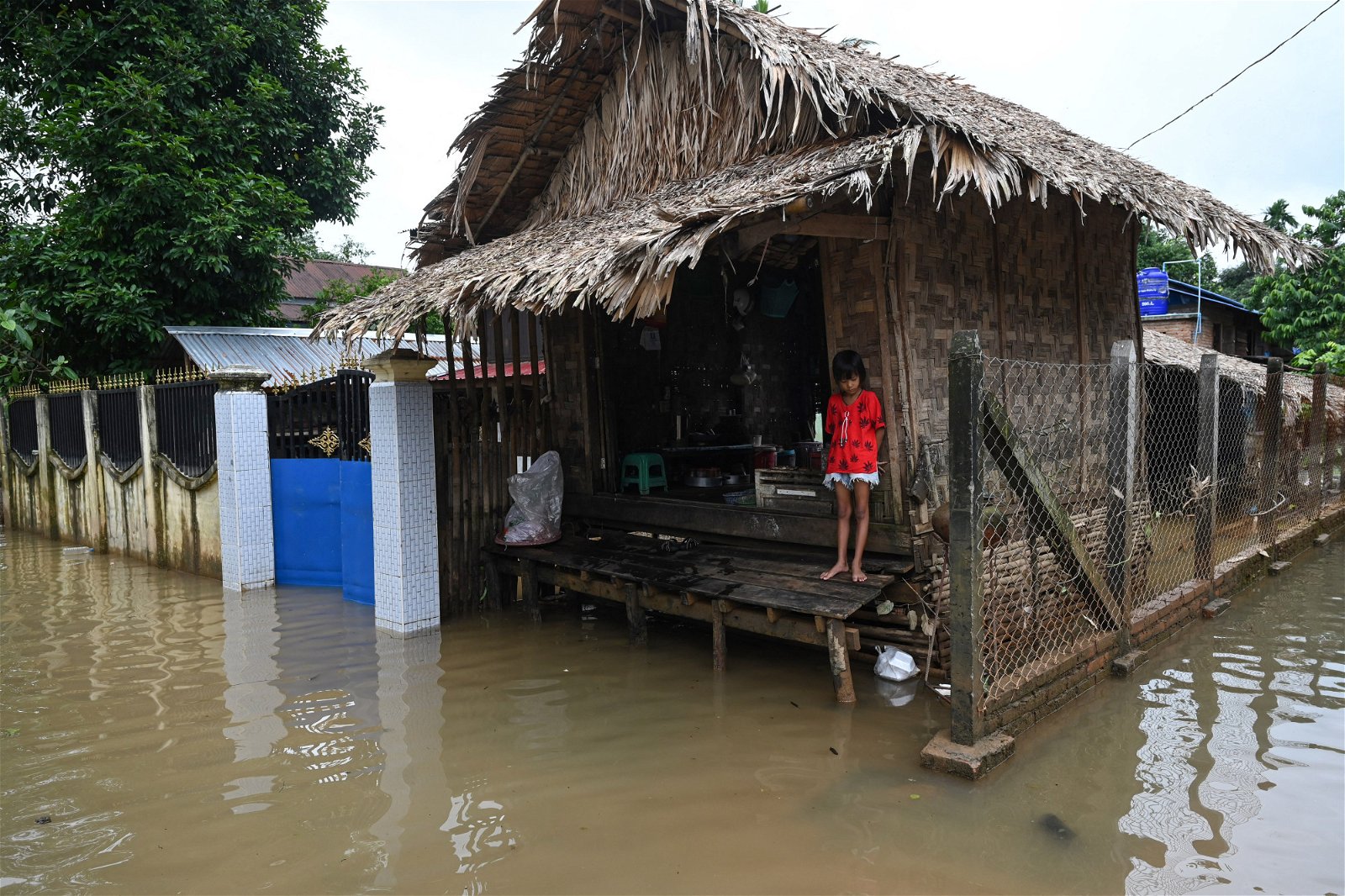 一名女孩站在家门前，面对被洪水淹没的屋子四周一筹莫展。（图取自法新社）